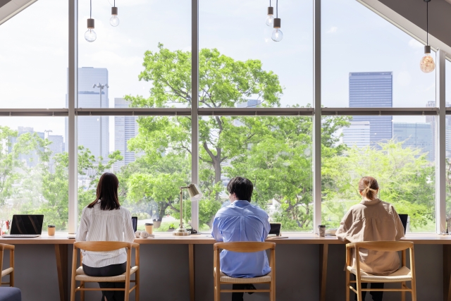 窓沿いに設置されたデスク 窓際で三人並んで仕事をしている